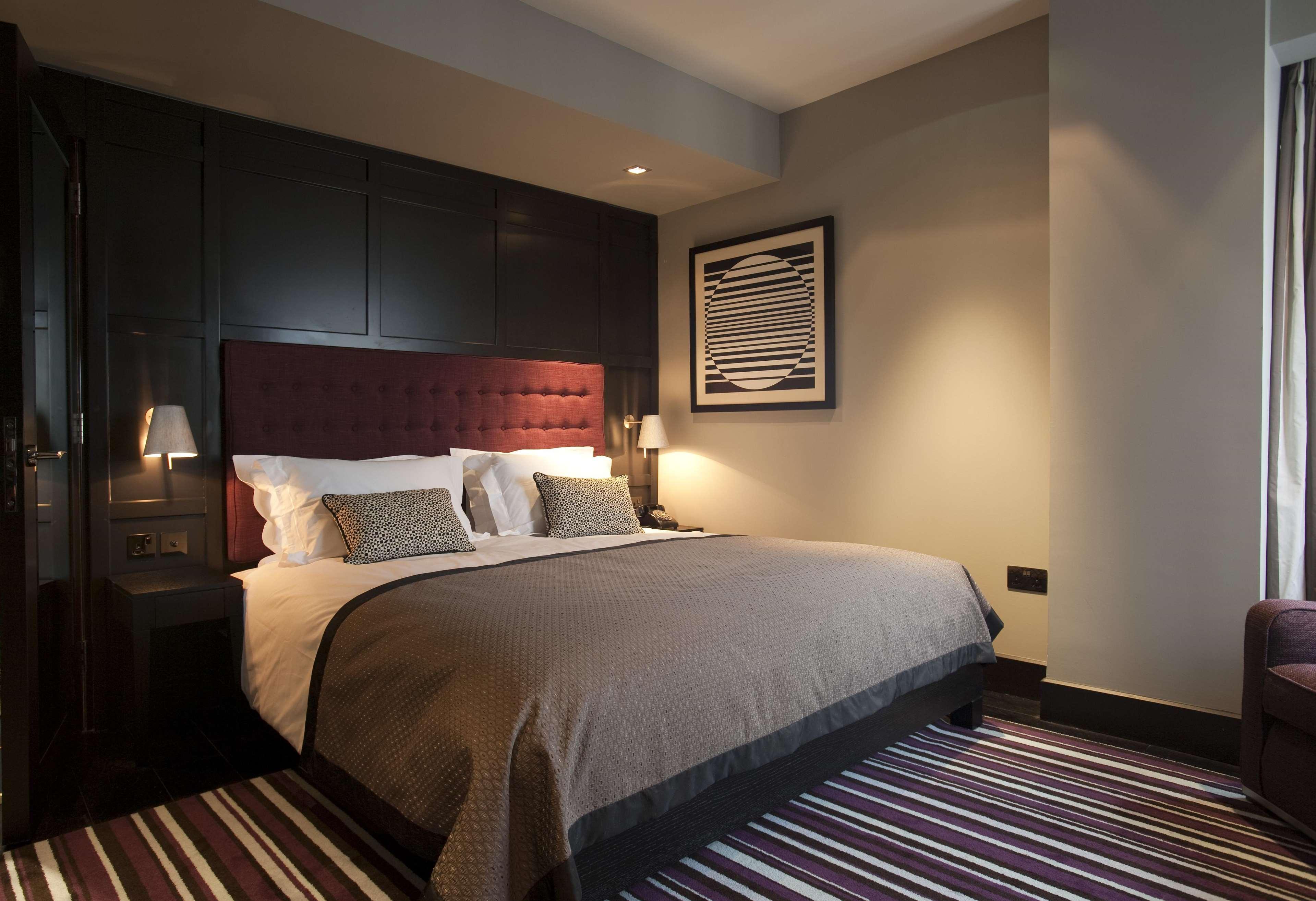 The Fitzwilliam Hotel Belfast Exteriér fotografie The photo shows a stylish and modern hotel room. It features a large bed with a tufted headboard in a deep burgundy color. The bed is dressed with neutral-toned bedding and decorative pillows. On either side of the bed, there are small bedside lamps 