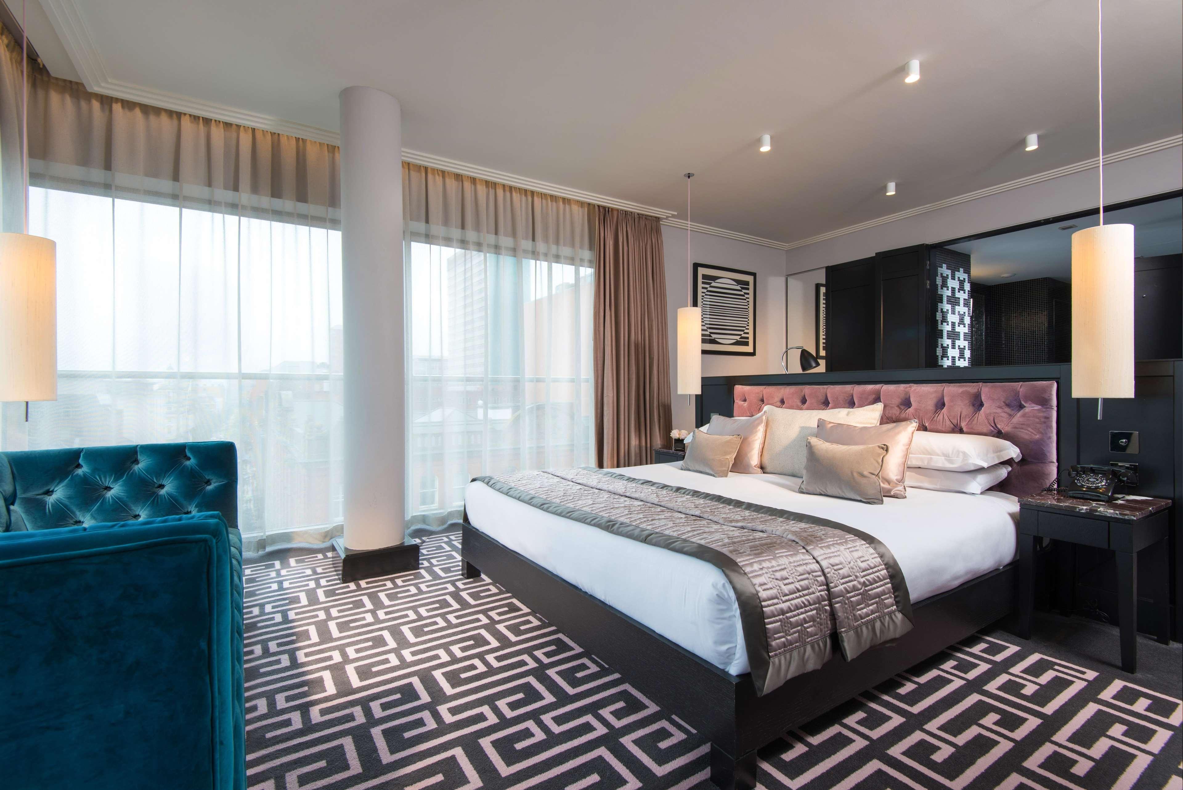 The Fitzwilliam Hotel Belfast Exteriér fotografie The photo showcases a modern hotel room. It features a large bed with plush pillows and a stylish headboard. The room has large windows with sheer curtains, allowing natural light to filter in. The floor is covered with a patterned carpet that contra