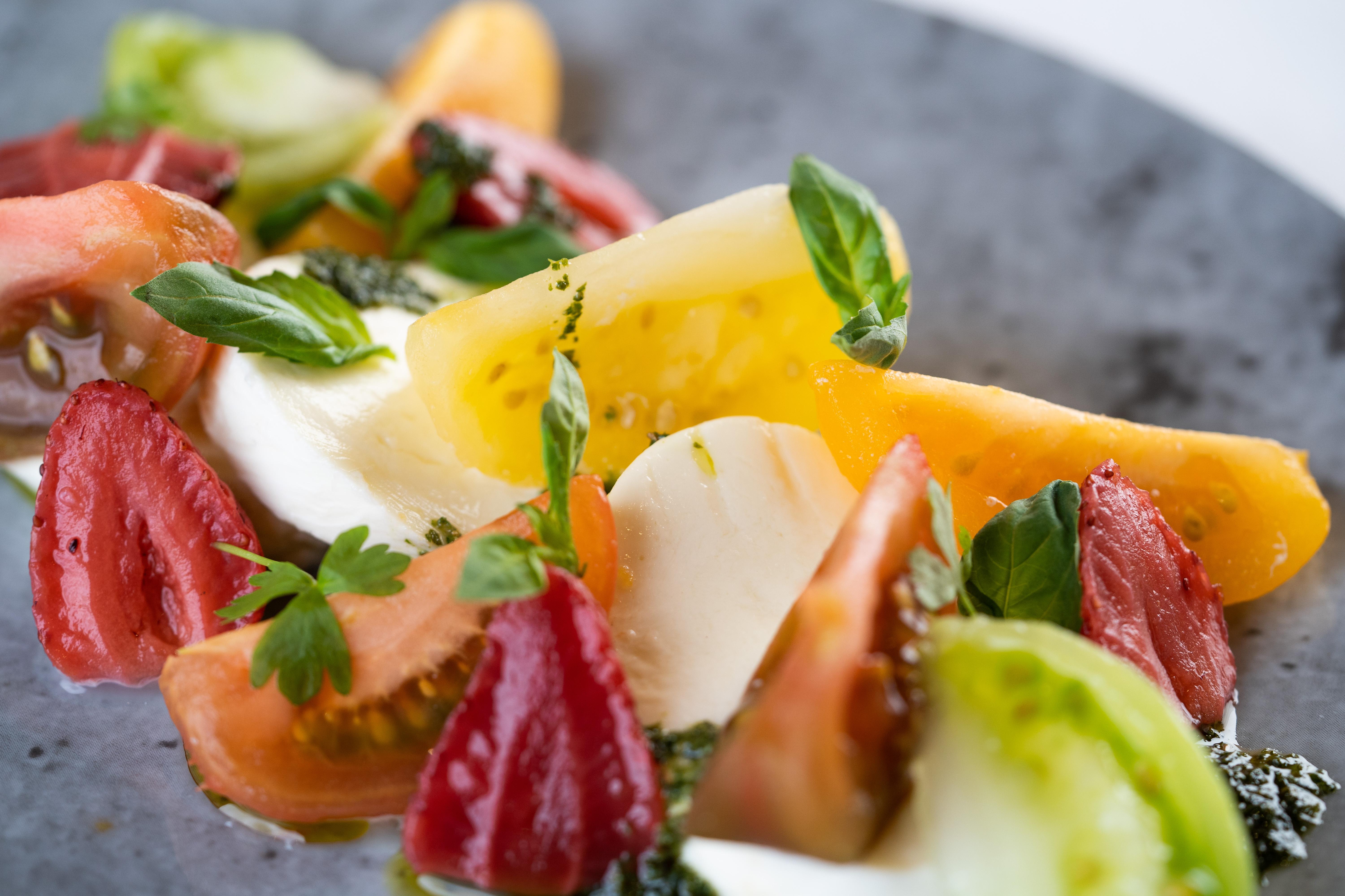 The Fitzwilliam Hotel Belfast Exteriér fotografie The photo shows a vibrant salad featuring slices of various tomatoes, including red, yellow, and green varieties. The tomatoes are paired with fresh mozzarella cheese and garnished with basil leaves. The dish is presented on a round, dark plate, high