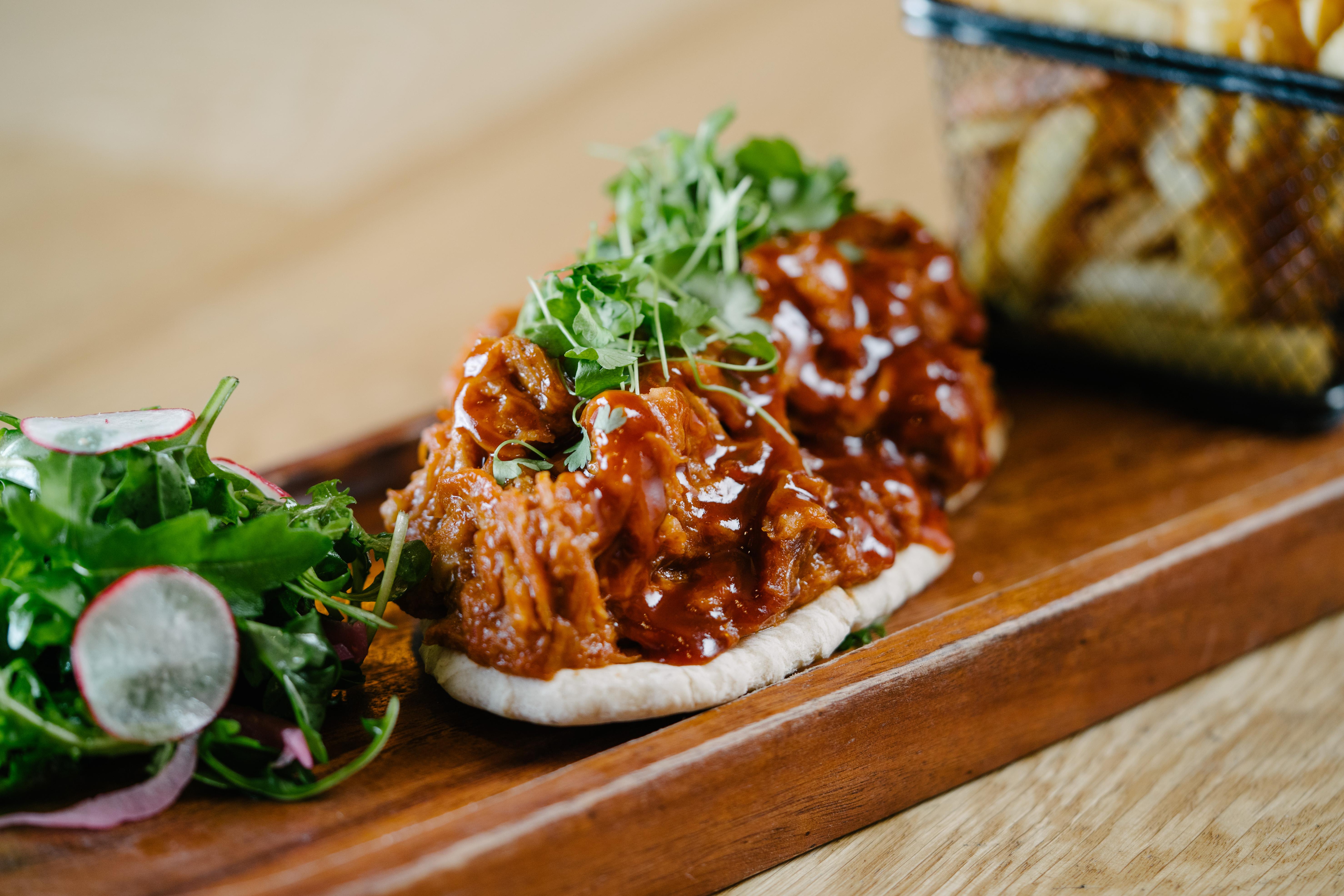 The Fitzwilliam Hotel Belfast Exteriér fotografie The photo shows a wooden platter featuring two pieces of bread topped with pulled meat covered in a rich barbecue sauce. The dish is garnished with fresh greens, including sprouts. On the side, there is a small serving of mixed salad with radishes an